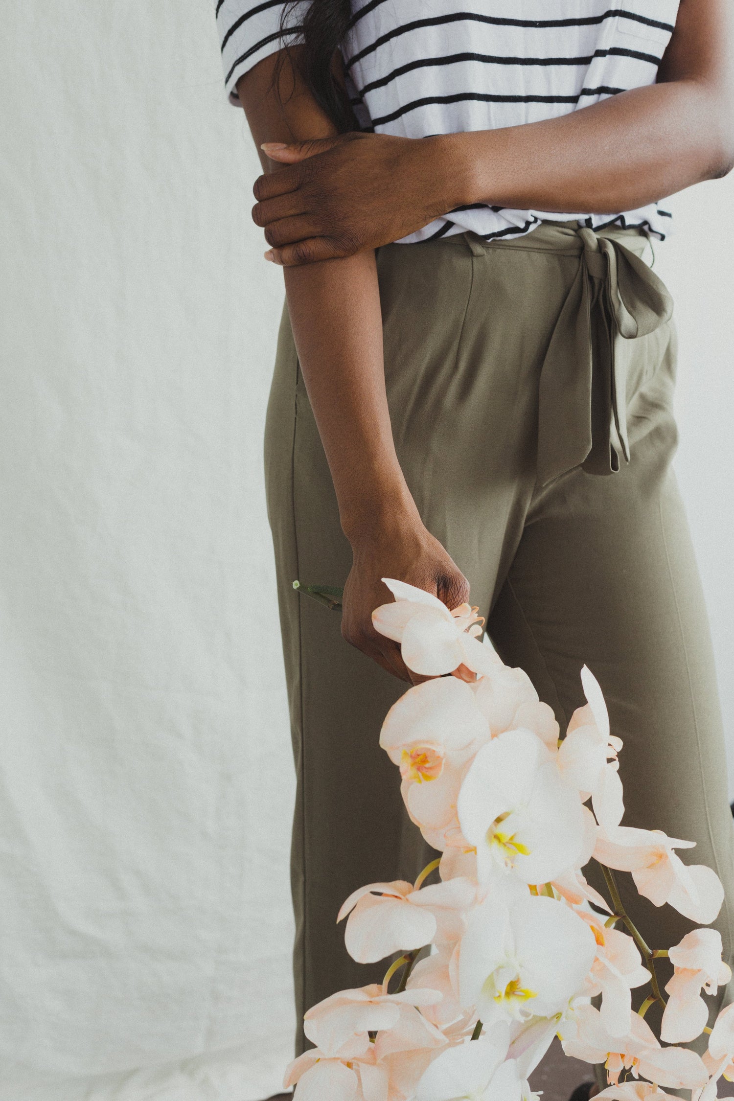 fashionable woman, who is wearing striped tshirt and drawstring flow pants, while holding a stem of orchids