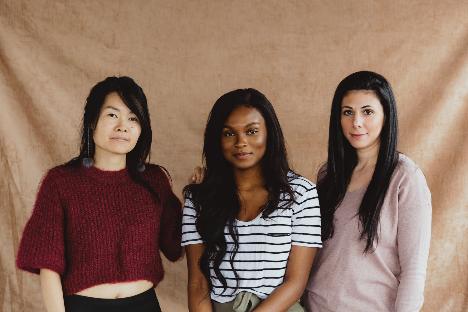 three fashionable women standing together in front of a pink backdrop