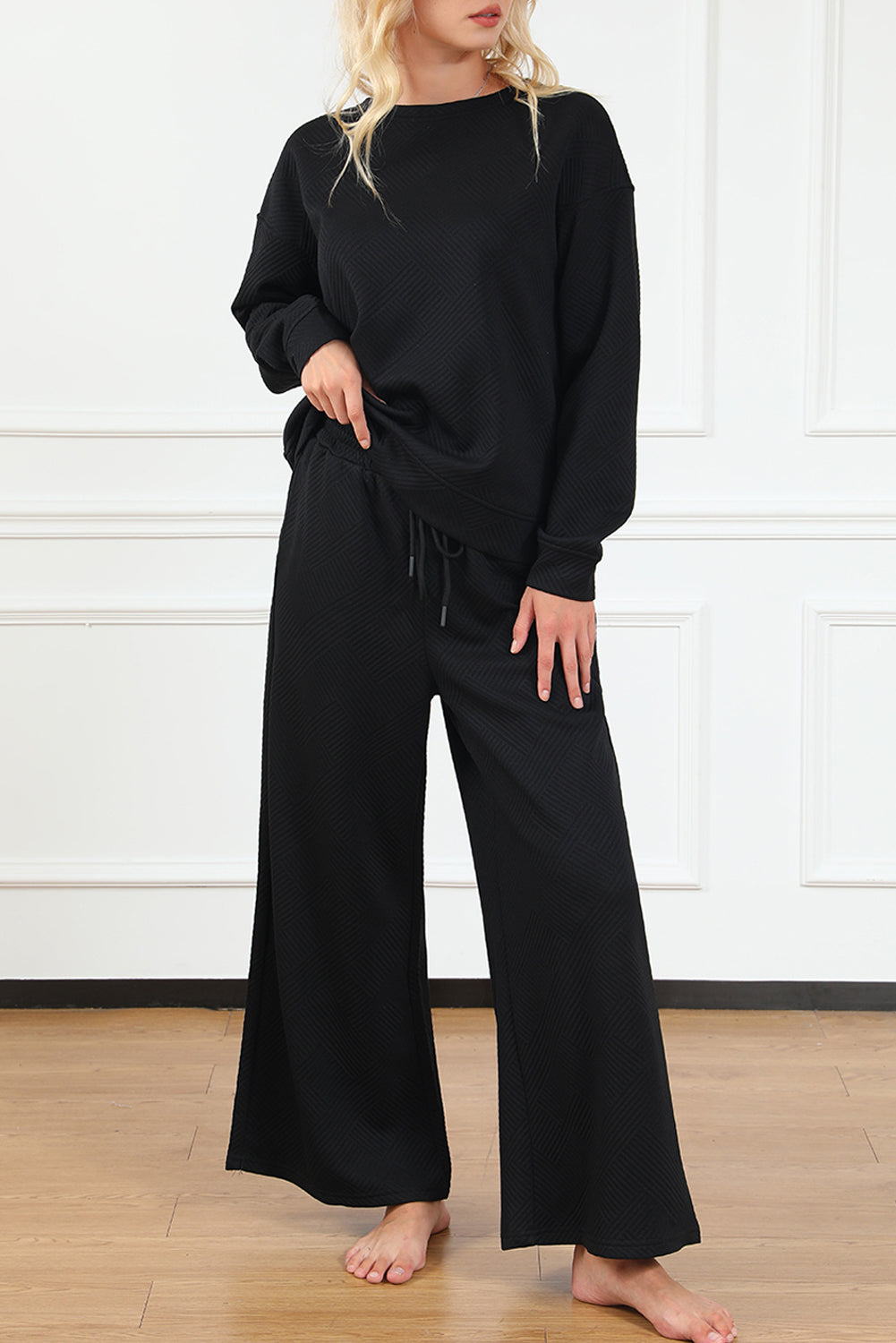 A woman wearing a Black Ultra Loose Textured 2-piece Slouchy Outfit, featuring a comfortable long-sleeved top and wide-leg pants with drawstrings, perfect for a laid-back, stylish look.