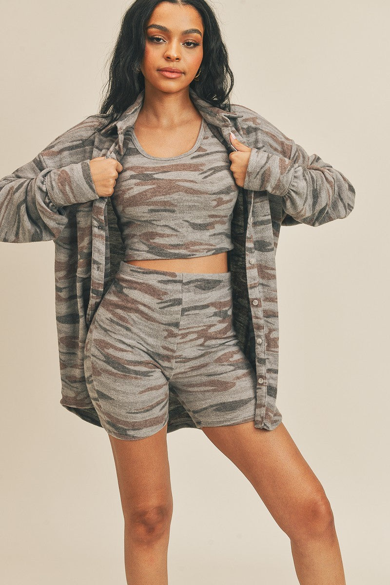 A woman is wearing a stylish three-piece camo set that includes a fitted tank top, high-waisted biker shorts, and a long cozy cardigan, perfect for lounging or casual outings.