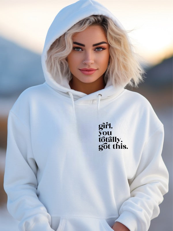 A young woman wearing a white hoodie with the motivational text "Girl, you totally got this" printed on the front in small, bold black letters. The hoodie features a cozy fit with a drawstring hood, ideal for a casual, confident look.